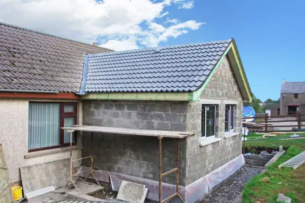 Agrandissement maison sur le côté en cours de construction, murs en parpaings, nouveau toit gris, échafaudage.