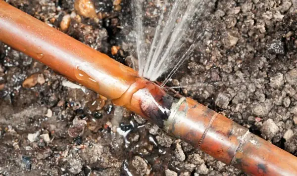 Une fuite sur un tuyau de cuivre, l'eau jaillit d'une fissure dans le sol.