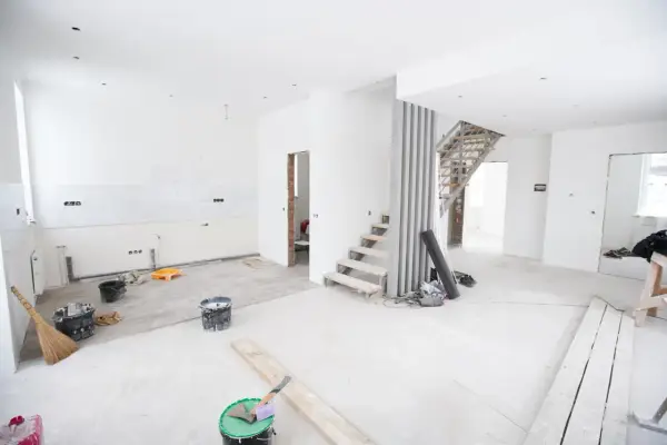 Chantier en cours pour rénover ma maison : escalier, seaux de peinture, balai et matériaux au sol.