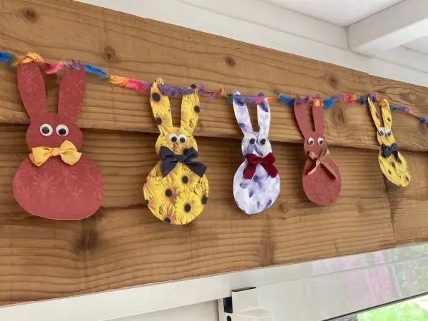 Guirlande de lapins colorés, déco de Pâques à faire soi-même avec récup. Des lapins en papier aux motifs variés, ornés de nœuds et d'yeux mobiles, suspendus à une ficelle multicolore.