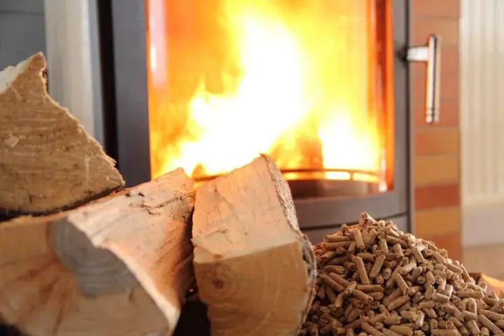 Bûches et granulés de bois prêts pour le chauffage au bois, avec un poêle crépitant en arrière-plan.