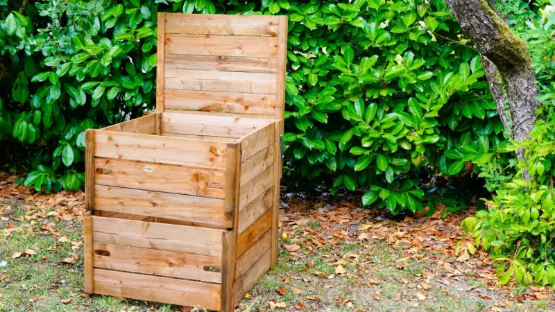 Un composteur en bois, prêt à l'emploi, est installé dans un jardin verdoyant. Idéal pour fabriquer un composteur maison.